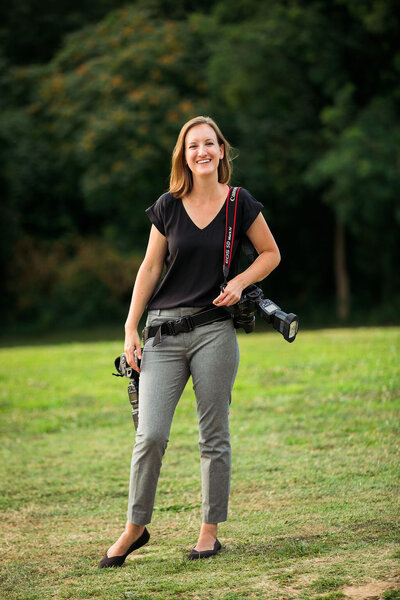 A photographer smiling with a camera hanging from her shoulder