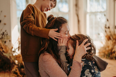 Mother sits between two boys embracing and giving a forehead kiss