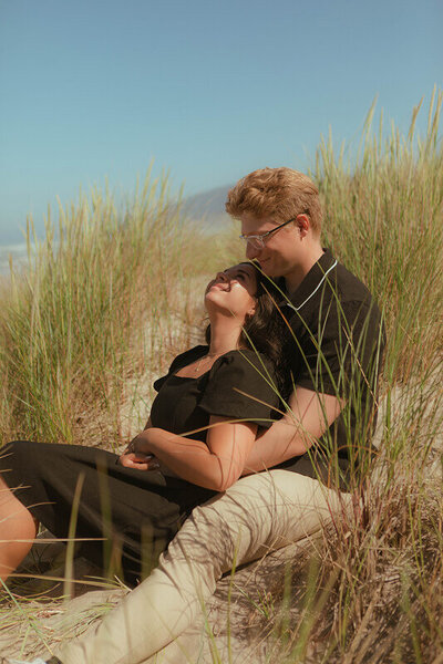 A woman sits between the legs of her boyfriend. She looks up at him as he looks down at her.