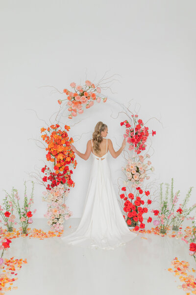 Bridal portrait at indoor wedding surrounded by bright orange, pink and red florals