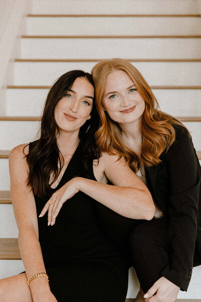 duo of women smiling at camera while sitting on stairs