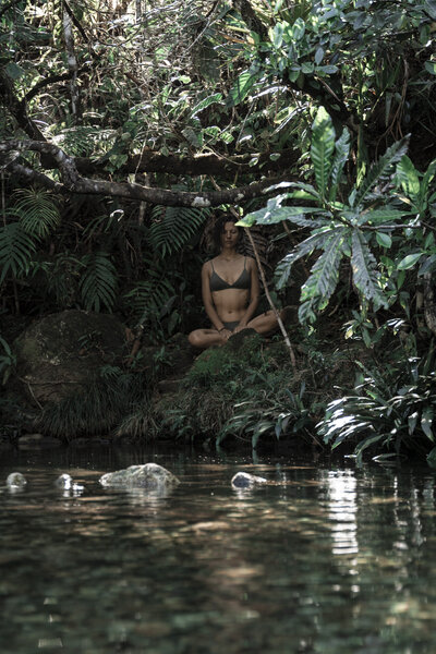Una mujer hace meditación en la selva con un río