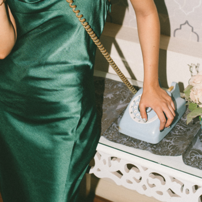 Woman wearing a green dress, leaning on a table and talking on the phone.