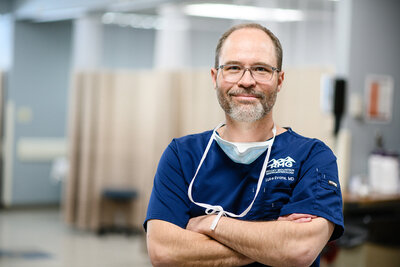 Business branding photography with a doctor standing in scrubs smiling at the camera with an operating room in the background