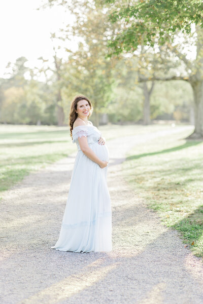 Mother-to-be smiles while holding her pregnant belly in Waveny park maternity session
