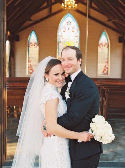 Bride and groom posing in front of wedding ceremony floral arrangement with pink flowers and green accents