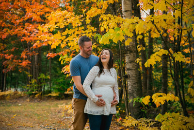 Couple standing with Fall Trees holding woman's belly |  Maternity Photography Session