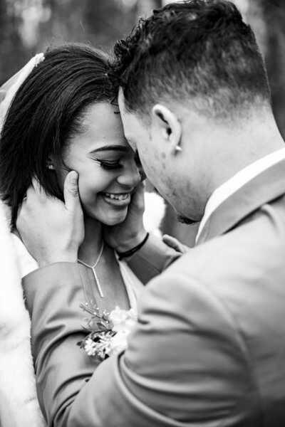 Black and white shot of the groom gently holding the bride's face as she smiles during bridal portraits at Kincaid Manor, capturing a tender moment.