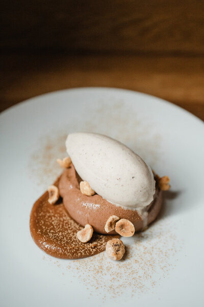 Dessert with chocolate mousse, quenelle of ice cream, hazelnuts, and sauce on a white plate.