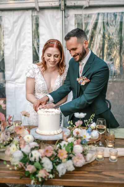 A bride and groom smile while cutting their cake, representing an example of film wedding photography by Among the Oaks. 