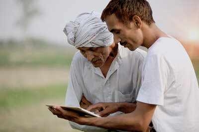 two men holding laptop in field