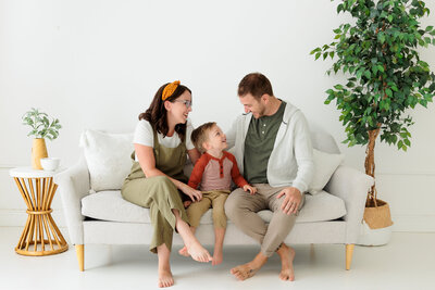 Mom and dad sit on sofa with son while everyone looks at each other