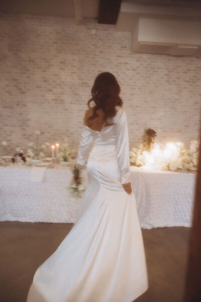 A person in a wedding dress walking towards a reception table.