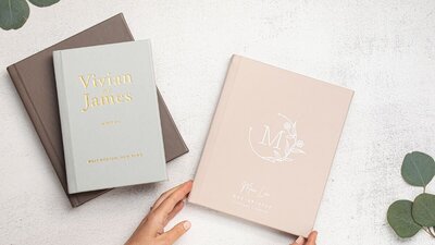 Custom wedding albums designed in difference colors and textures, showing options like light blue with gold foil lettering and pink canvas binding.