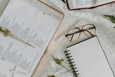 Flat lay of open Bible, notebook, glasses, and flowers