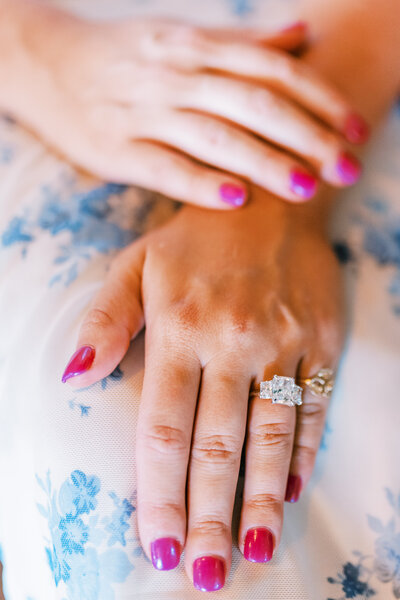 Close up image of a woman's hands with a large diamond ring and pink nail polish