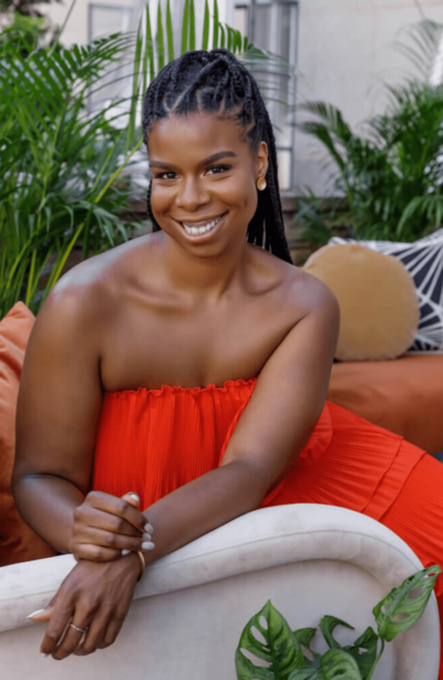 Fallon Carter, founder of The We Do Collective, smiling in a vibrant red dress while seated at 620 Loft and Garden. She is surrounded by lush greenery, creating a relaxed and elegant atmosphere.