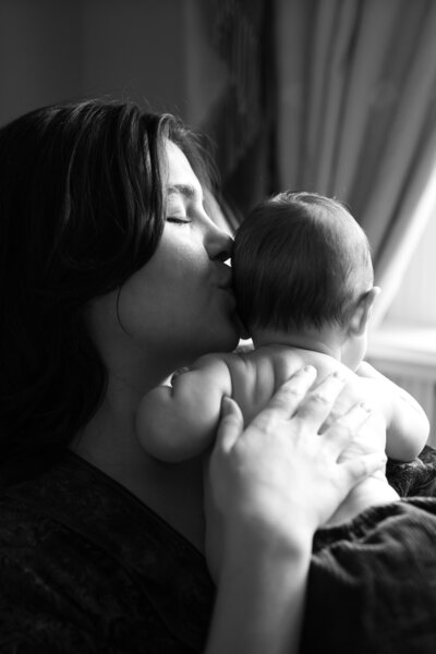 Mum holds her newborn baby  to her shoulder as she kisses her head