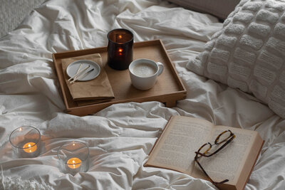 A book, latte, and candle resting peacefully on a cozy white bed.