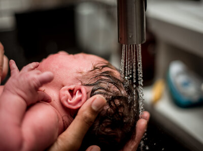 Newborn’s hair being gently rinsed under warm water at home