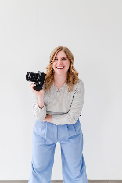 Image of Brook standing on one foot, holding her camera and smiling.