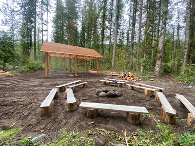 Fire pit surrounded by wooden benches and a pavilion in the background