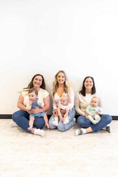 Three mothers sitting on the floor smiling while holding their babies