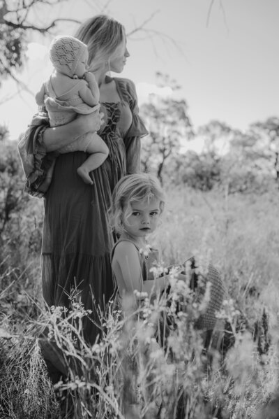 A woman and a young child sit together in a field of red flowers, with the woman holding the child's hand.