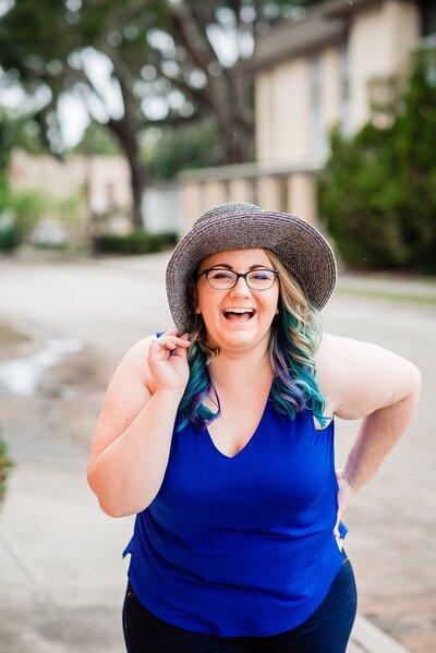 Wedding photographer wearing blue top and laughing at camera while wearing a sunhat