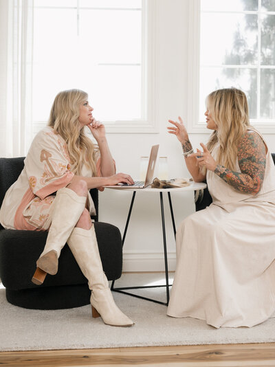 two women sitting at table talking with a laptoo