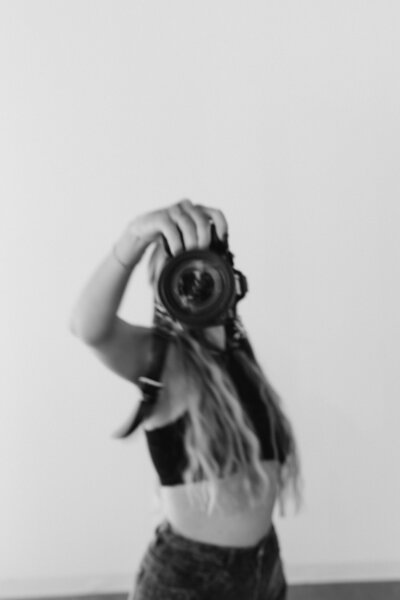 Black & white image of Courtney, the owner, walking with her camera