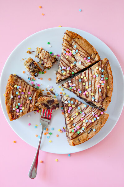 a cookie cake topped with sprinkles and chocolate drizzle