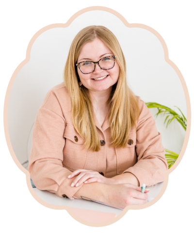 headshot photograph of blonde brand design business owner wearing glasses smiling at the camera and wearing tan jacket.