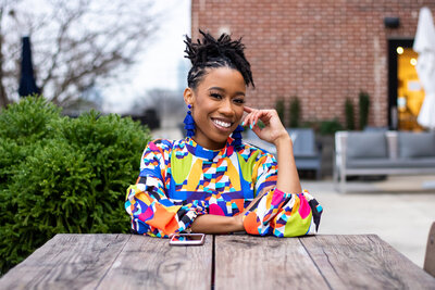 black woman sitting outside at table in colorful dress