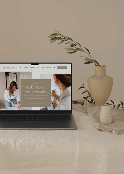 Laptop met de website van Listing & Living open, gepresenteerd met natuurlijke styling en keramische vaas op linnen tafelkleed