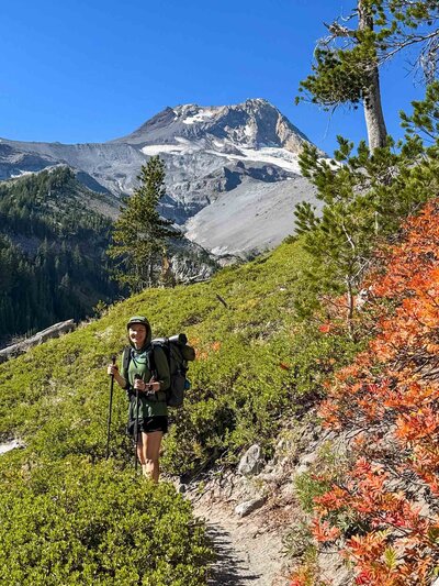 a backpacker holding trekking poles and wearing a backpack with Mount Hood as a backdrop