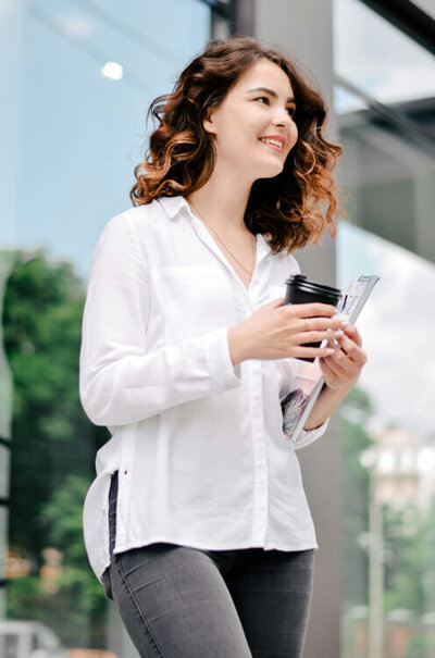 Woman in a white shirt smiling and holding a coffee cup