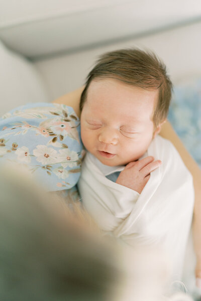 a sweet swaddled newborn sleeps in his mothers arms.