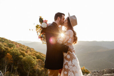 Groom picks up bride for celebratory kiss after forest elopement ceremony. She holds her feet up and her bouquet behind his head.