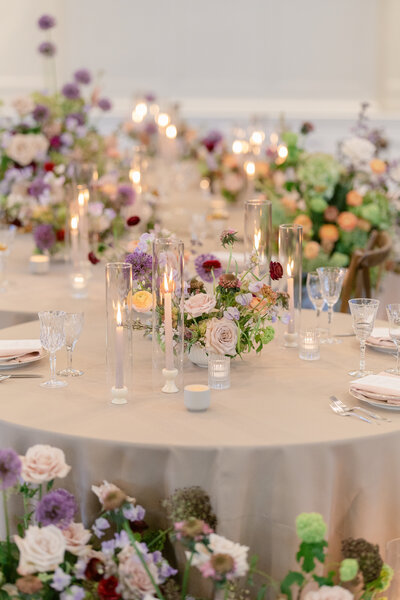 A close up photo of round wedding tables styled with purple, peach and green florals.