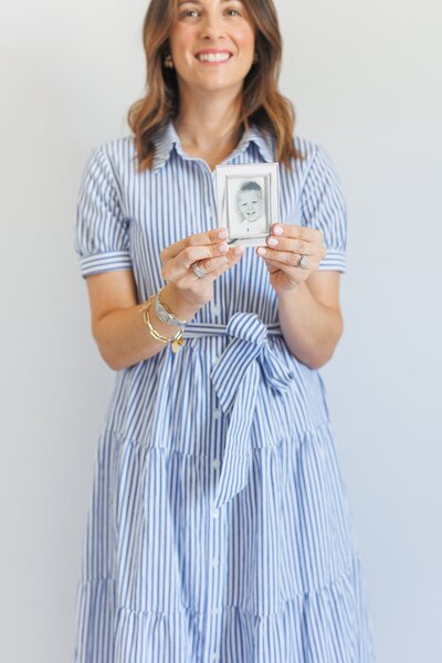 Woman in a striped dress holding a framed child’s portrait.