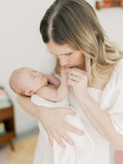 A mother holds her newborns hands and kisses them during her Austin newborn photo session