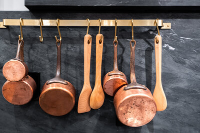 copper pots and wooden spoons hanging on a bar