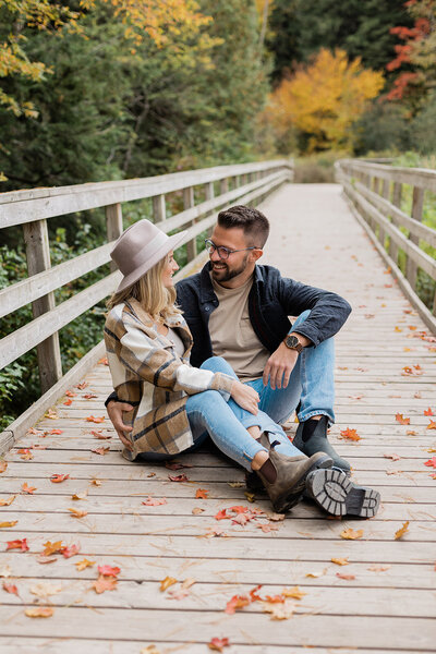 Couple sitting on a bridge in fall smiling
