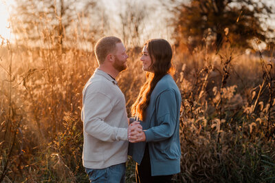 A couple faces each other smiling and holding hands.