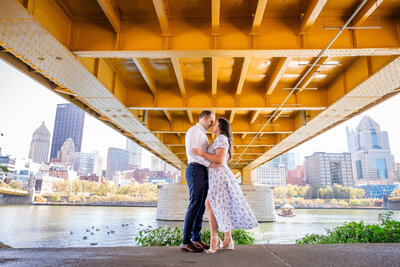 picture of a couple under the and warhol bridge in pittsburgh with the city skyline