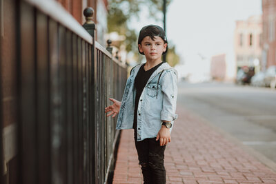 model boy holding onto fence while getting his pictures taken. 