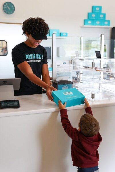 Authentic lifestyle branding image showcasing the atmosphere of a local donut shop. The photo captures the warmth of the space, the artistry of the donuts, and the joy of customers enjoying their treats, highlighting the brand’s inviting and community-focused vibe