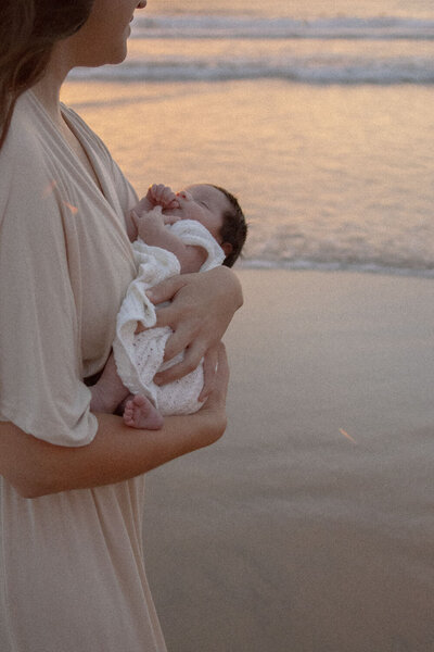 Mother holding her newborn baby at sunset by the beach