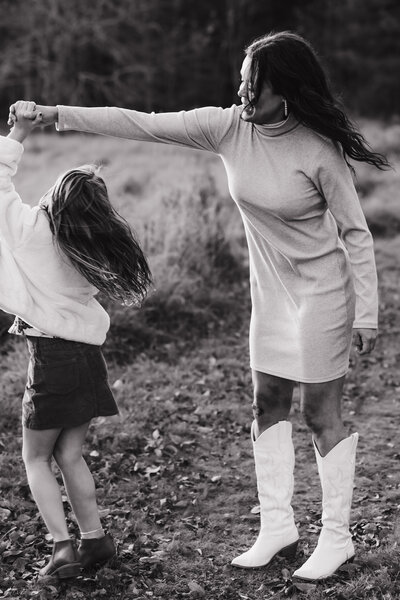 a black and white photo of a mom holding her daughters hand and twirling her around